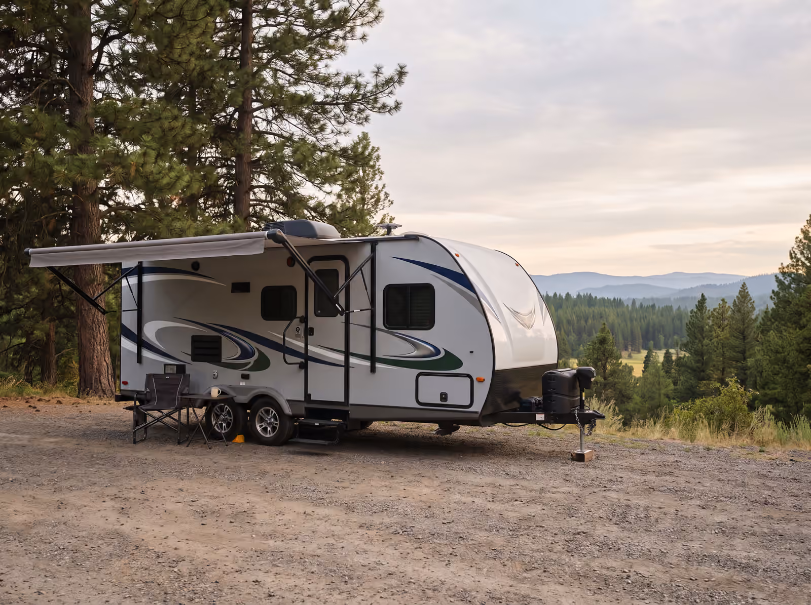 A travel trailer parked at a forested overlook with its awning out